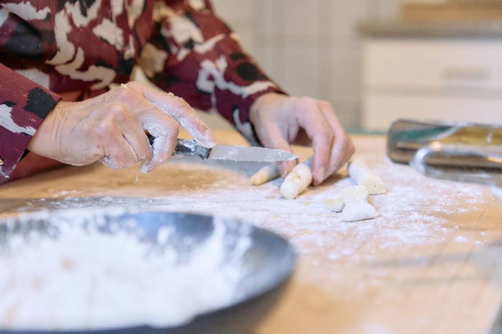 Des mains travaille une pâte. Elle coupe des bouts. La personne porte une chemise colorés. Mais on voit que ses mains