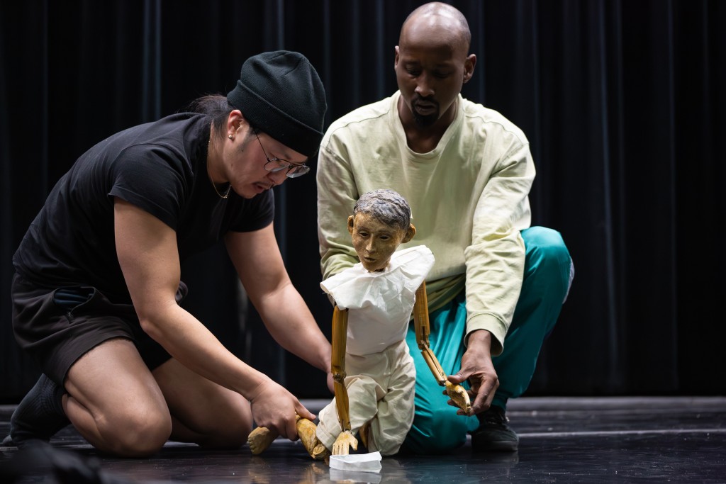 Deux personnes assise par terre en train de manipuler une marionnette. La marionnette est habillée en blanc.