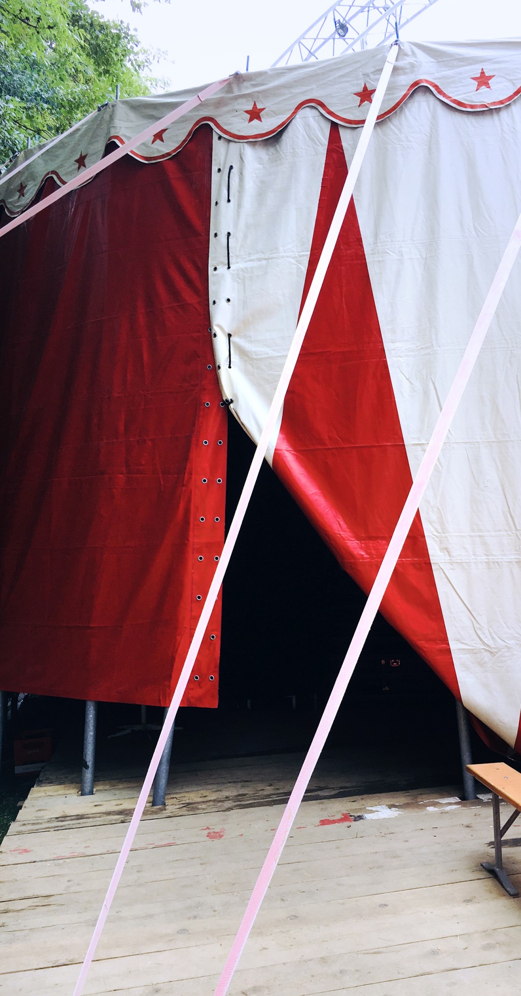 C'est l'image d'une partie de la tente d'un cirque. Donc un lourd rideau un peu ouvert rouge et blanc et des pots qui soutiennent la structure. C'est pas vraiment l'entrée du cirque, mais plutôt une partie de la tente qui se souleve.